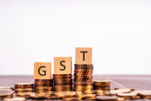 GST Government Sales Tax on Wood Block with Stack of Coins